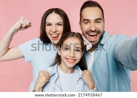 Close up young happy fun parents mom dad with child kid daughter teen girl in blue clothes doing selfie shot pov on mobile cell phone do winner gesture isolated on plain pastel light pink background.
