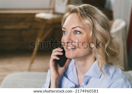 Beautiful woman is talking on the phone and smiling. Smile with teeth. Closeup portrait of blonde woman using phone. A girl with blue eyes uses a smartphone. Modern wireless communications
