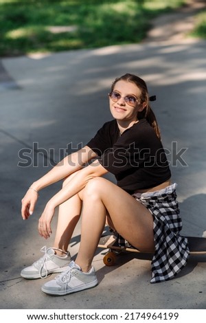 Teenager skater girl is sitting on skateboard on the skaters park