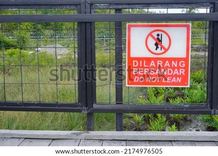 Inscription: It is forbidden to lean on the railing as a caution to the public in an outdoor room which is painted red with black text                            