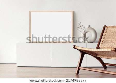 Blank picture frame mockup on white wall. Living room design. Empty white template copy space for artwork. View of modern scandinavian style interior with chair. Home staging and minimalism concept