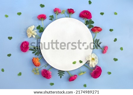 Pink and white flowers buttercups with paper card note with space for text on a blue background. Top view, flat lay