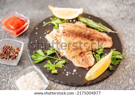 Baked white fish fillet Pangasius with spices and lemon on a stone background
