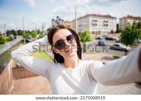 pretty young woman with a smile stands in the city after work and has fun, taking a light fun selfie on a blurred background
