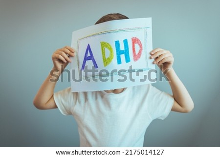 Young boy holds ADHD text written on sheet of paper. ADHD is Attention deficit hyperactivity disorder. Close up. Boy holding paper and admitting suffering from ADHD. Royalty-Free Stock Photo #2175014127