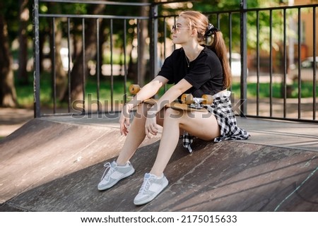 Teenager skater girl is sitting and resting on the ramp in the skate park