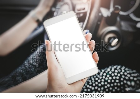 female hand holds a mobile phone with a blank white screen in the car interior. mockup. copy space