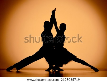Couple of dancers are dancing elements of Argentine tango. Black silhouettes of man and woman on an orange brown gradient background in studio. Screensaver for school of ballroom Latin American dances Royalty-Free Stock Photo #2175035719