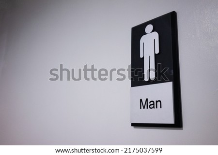 Male toilet sign on a white wall in a dimly lit room.