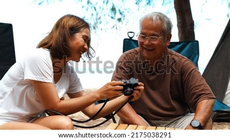 Happy family older senior father and daugther looking picture in camera taking memories outside on the beach camping together fun and enjoy life.