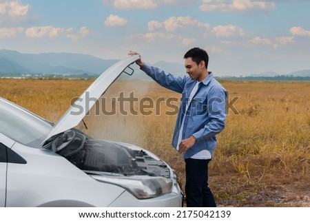 Overheated car and engine broke with breakdown radiator steam and hot oil smoke from under the hood. Asian young man auto driver standing open car hood on outdoors. Automobile motor problem concept. Royalty-Free Stock Photo #2175042139