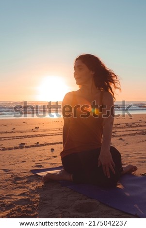 silhouette of a woman on the beach practicing a stretching exercise at sunset. vertical