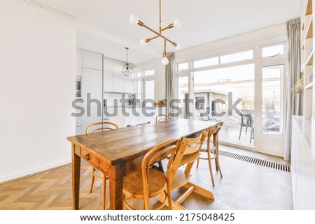 Interior of spacious light dining room with elegant chandelier located near kitchen with comfortable furniture and appliances