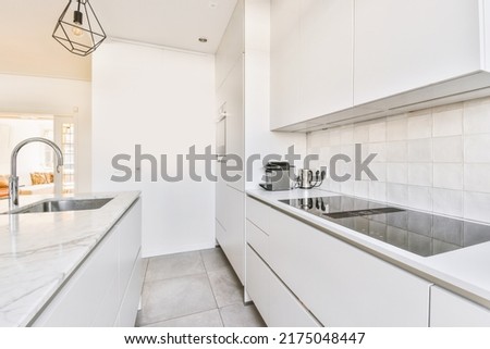 Interior of spacious light dining room with elegant chandelier located near kitchen with comfortable furniture and appliances