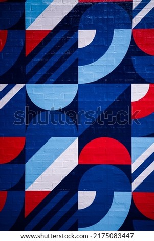 Red, white and blue geometric mural with shapes and lines in a block containments on brick texture.
