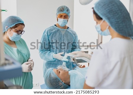 Doctor anesthesiologist holding breathing mask on patient face during operation