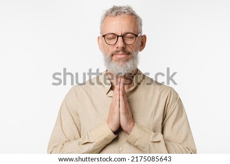 Relaxed resting caucasian mature middle-aged man in beige shirt praying meditating feeling zen-like with eyes closed, doing breathing exercises isolated in white background