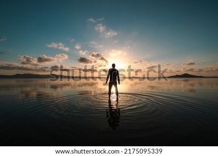 Silhouette of a man standing with his back facing at sunset over the shallow waters of the Mar Menor, Region of Murcia, Spain, creating ripples on the surface of the water Royalty-Free Stock Photo #2175095339