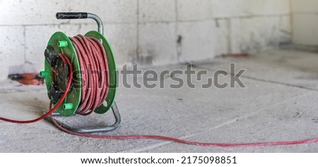 Red and green power cord extension lead drum on construction site ground, closeup detail with empty space for text right side Royalty-Free Stock Photo #2175098851