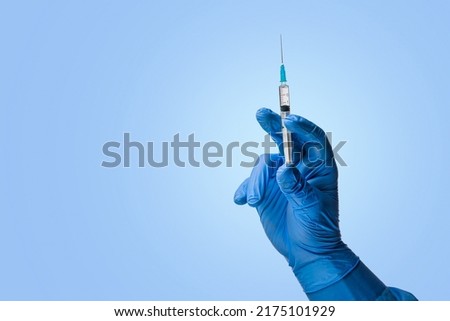 Doctors hand in surgical gloves holds a syringe on a classic symbolic blue background Royalty-Free Stock Photo #2175101929