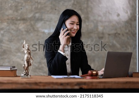 Attractive young lawyer or Businesswoman talking on phone and lawyers discussing contract papers with brass scale on wooden desk in office. Law, legal services, advice, Justice and real estate concept