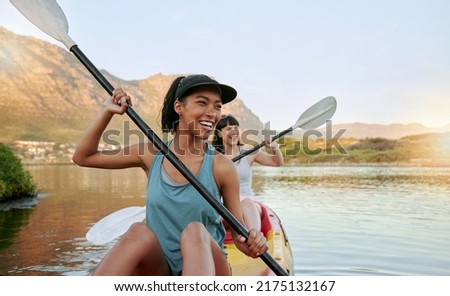 Two smiling friends kayaking on a lake together during summer break. Smiling and happy playful women bonding outside in nature with water activity. Having fun on a kayak during weekend recreation Royalty-Free Stock Photo #2175132167
