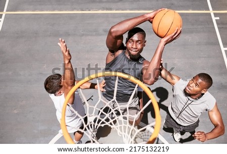 Basketball players blocking a player from dunking a ball into net to score points during a match on sports court from above . Fit athletes jumping to defend in competitive game for recreational fun