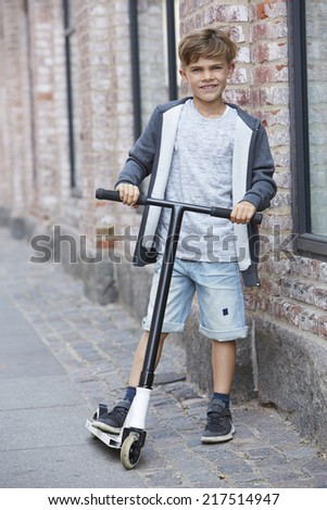 Portrait of young boy with scooter on sidewalk 