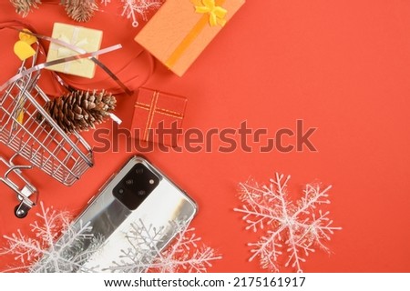 shopping cart and smartphone with three cameras, christmas decor on a red background, gifts boxes, snowflakes and phone, christmas and new year discounts and gifts concept
