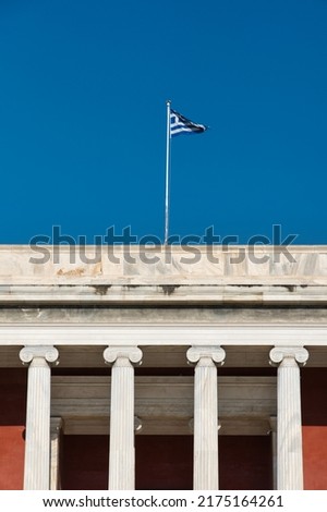 Impressive old building with massive columns with a greek flag on the roof in front of a perfect sky with small clouds. Abstract tranquil scene. 