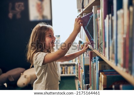 Schoolgirl choosing book in school library. Smart girl selecting literature for reading. Books on shelves in bookstore. Learning from books. School education. Benefits of everyday reading Royalty-Free Stock Photo #2175164461
