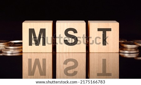 MST text on wood cubes with coins, black background, business concept. the inscription on the cubes is reflected from the surface of the black table. front view. MST acronym