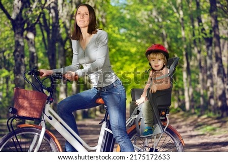 Mother with little blond boy on e-bicycle on backseat on the alley in the park Royalty-Free Stock Photo #2175172633