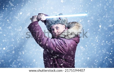 Man in winter clothes with a wooden light sword in his hands on a blue background with falling snow.