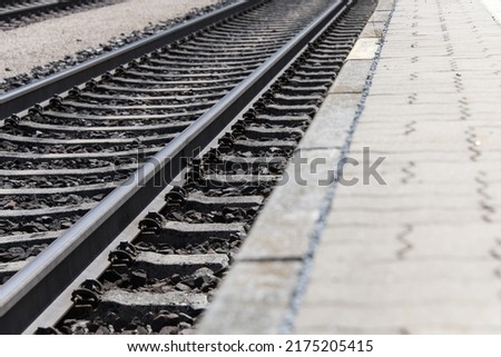 Ground view of railroad tracks running diagonally through the image with partially visible platform as a concept for train travel stations and railroad traffic Royalty-Free Stock Photo #2175205415