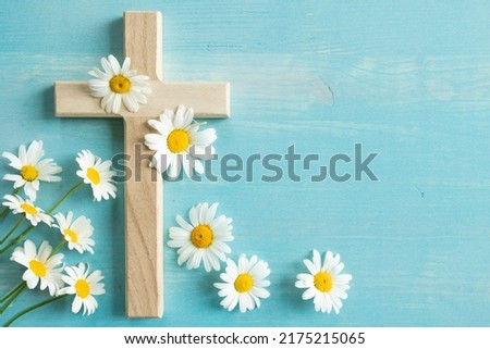 Daisy flowers on Christian wood cross on a blue wood background with copy space