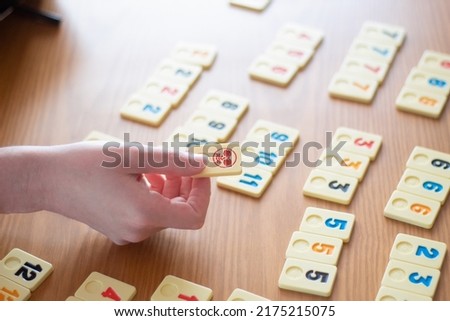 Hand holding a Joker tile over a game of Rummy in progress on a table with natural light streaming in