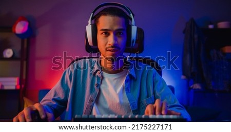 Happy asia guy gamer wear headphone participation play video game colorful neon lights computer in living room at night modern house. Esport streaming game online, Home quarantine activity concept. Royalty-Free Stock Photo #2175227171