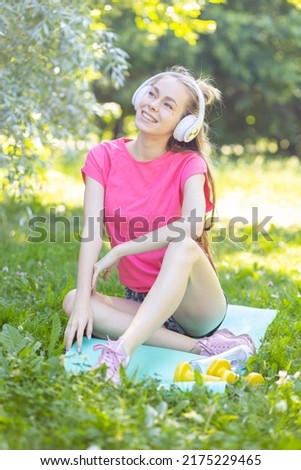 Beautiful young girl practicing yoga or fitness in summer in the park. Attractive female doing morning meditation, drinking water. Concept of healthy lifestyle, self care, wellness, work life balance