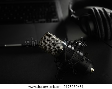 On a dark gray background, a laptop, studio headphones and a studio microphone. Radio, recording studio, audio work, podcast, vocal studio, journalism, blogging, home office.