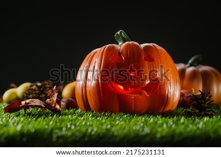 mystical composition. On a green lawn, a Halloween pumpkin with a carved face is illuminated from the inside by a candle against a spooky dark sky. Halloween, banner, holiday invitation.