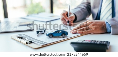 Man signing car insurance document or lease paper. Writing signature on contract or agreement. Buying or selling new or used vehicle. Car keys on table. Warranty or guarantee. Customer or salesman. Royalty-Free Stock Photo #2175244659