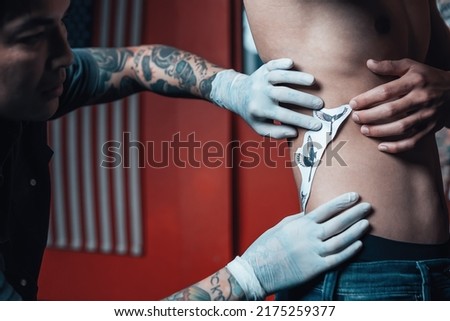 Skilled tattoo artist putting a sketch on the waist of a man before tattooing.