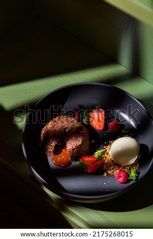 Brownie with caramel inside, a ball of walrus, strawberries, raspberries, pistachios and blueberries in a plate on a green table