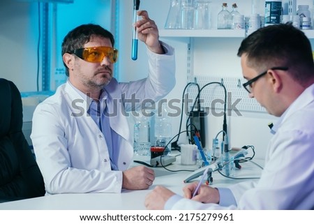 Male scientist in lab working in pharmaceutical studies and medical research with microscope and liquids in test tubes.