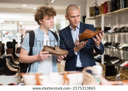 Shoe store employee helping teen to choose classic brown shoes in a shoe store Royalty-Free Stock Photo #2175313865