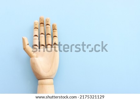 Wooden figure hand with happy faces on blue background.