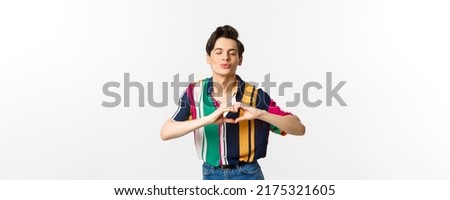 Lovely young man pucker lips and showing heart sign, waiting for kiss, I love you gesture, standing over white background