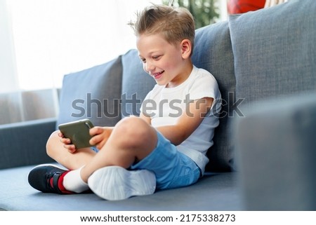 Little boy sitting on sofa at home and using smartphone