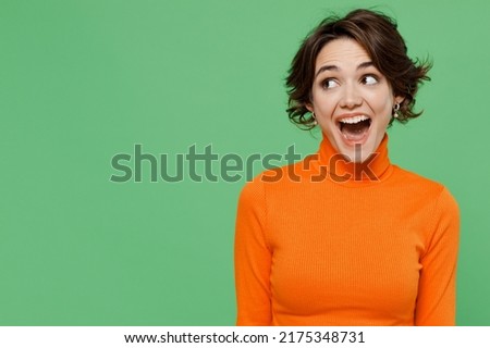Young amazed surprised fun woman 20s wear casual orange turtleneck look aside on workspace area mock up isolated on plain pastel light green color background studio portrait. People lifestyle concept